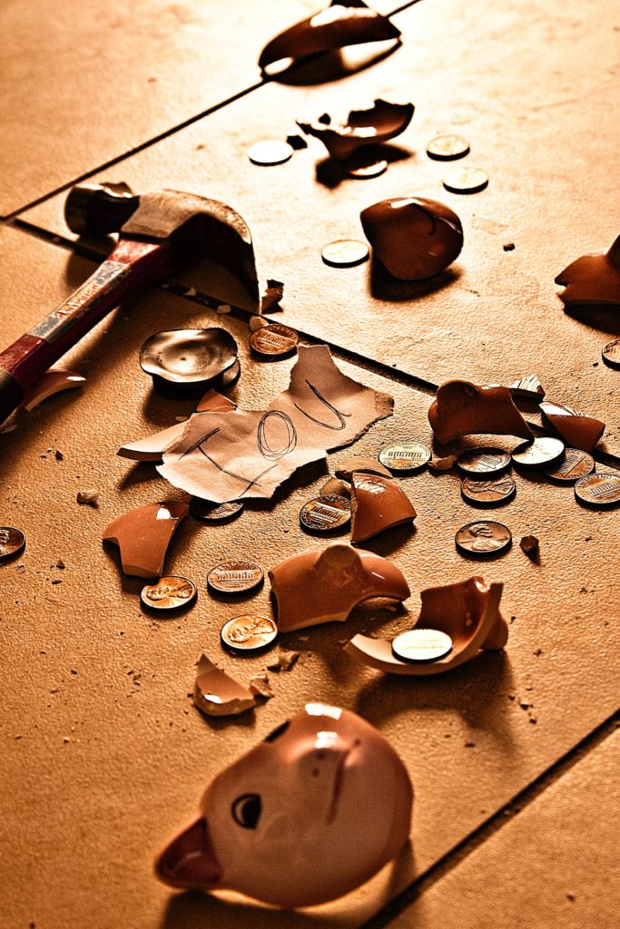 Broken ceramic pig shaped savings bank with coins strewn across floor and "IOU" note.